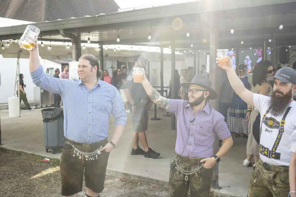 Three men raising beer mugs at outdoor event