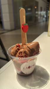 Chocolate covered strawberries in cup with a stick.