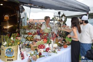 People browsing flower crafts at outdoor festival stall.