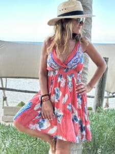 Woman in floral dress and sunhat by the beach.