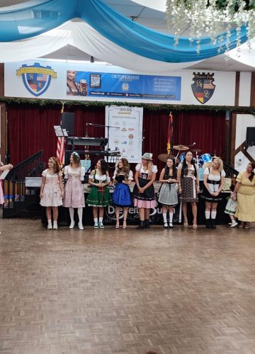 People in traditional outfits on stage at Oktoberfest event.