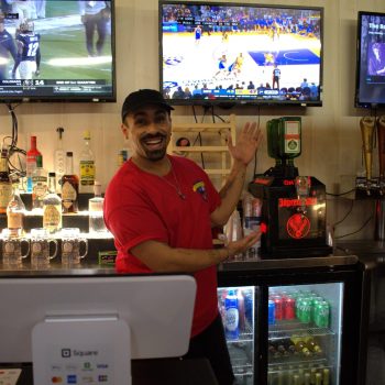 Bartender at bar with multiple TV screens.